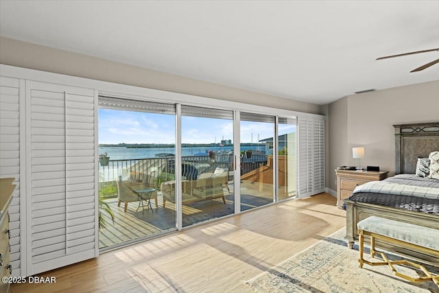 bedroom with access to exterior, a water view, and hardwood / wood-style flooring