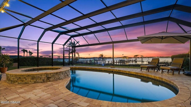 pool at dusk featuring glass enclosure, an in ground hot tub, and a patio