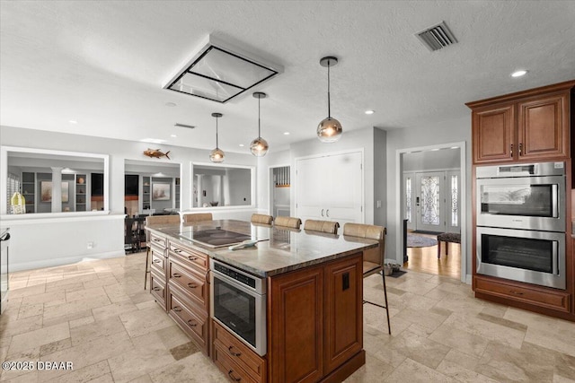 kitchen featuring decorative light fixtures, dark stone countertops, a kitchen island, a breakfast bar area, and stainless steel appliances