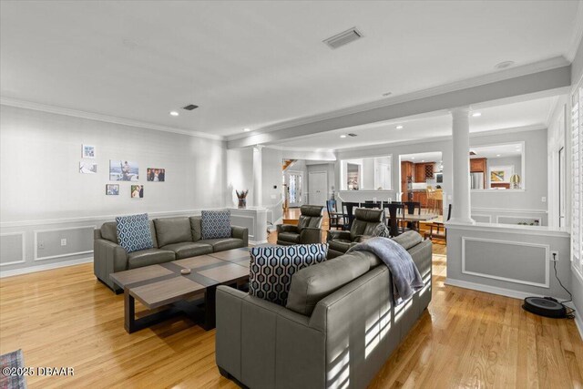 living room with light wood-type flooring, ornamental molding, and decorative columns