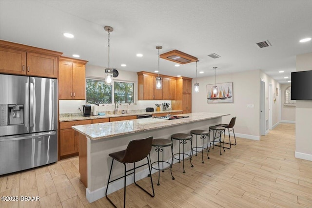 kitchen with light stone countertops, pendant lighting, stainless steel fridge with ice dispenser, and a kitchen island