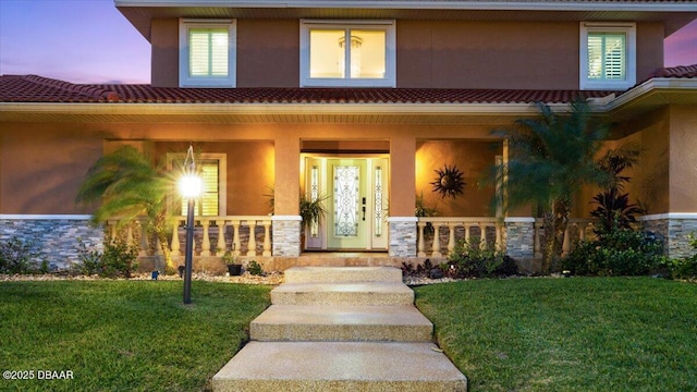 exterior entry at dusk featuring a porch and a yard