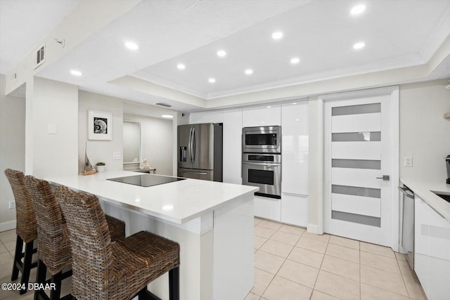 kitchen with kitchen peninsula, stainless steel appliances, a raised ceiling, white cabinets, and a breakfast bar area