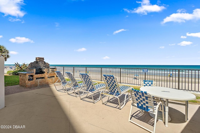 view of patio featuring an outdoor stone fireplace, a water view, and a view of the beach