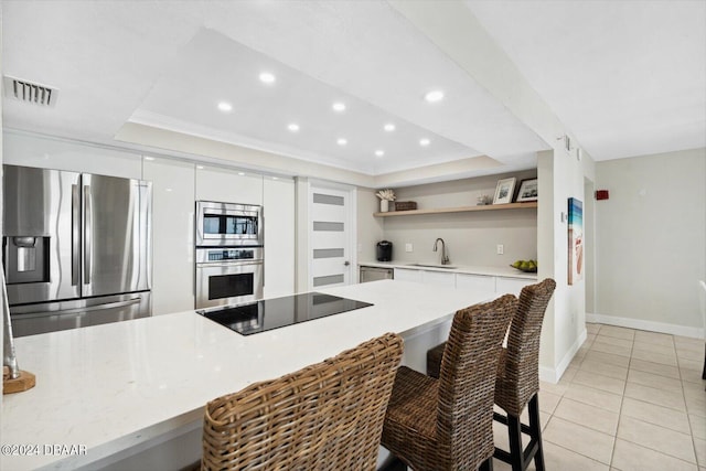 kitchen with appliances with stainless steel finishes, a raised ceiling, sink, white cabinetry, and light tile patterned flooring