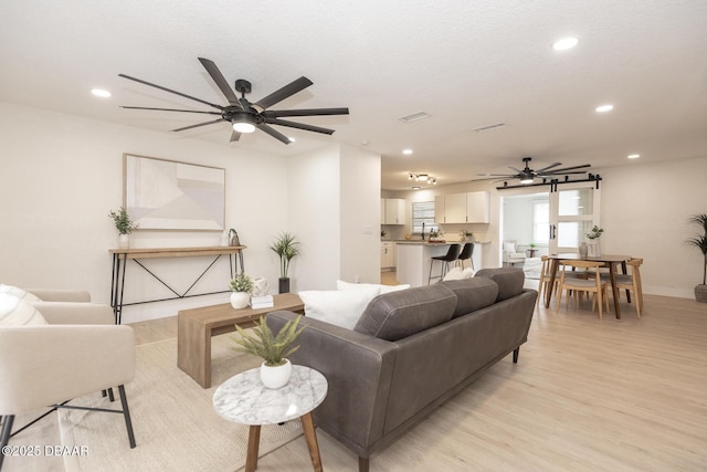 living room with ceiling fan, sink, light hardwood / wood-style floors, and a textured ceiling