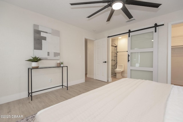 bedroom featuring ensuite bathroom, a walk in closet, a closet, ceiling fan, and a barn door