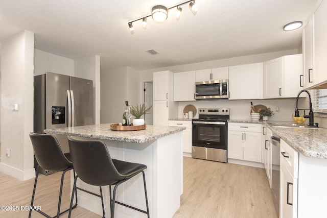 kitchen featuring stainless steel appliances, a center island, sink, and white cabinets