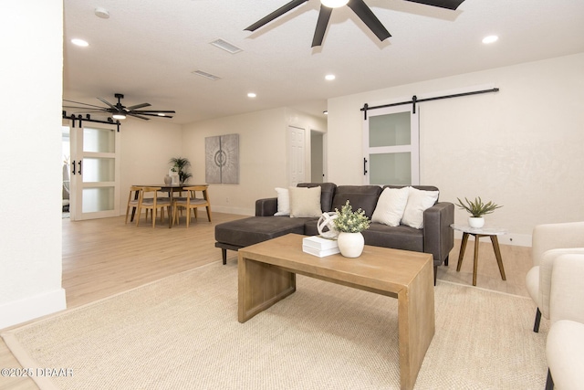 living room with ceiling fan, a barn door, and light hardwood / wood-style flooring