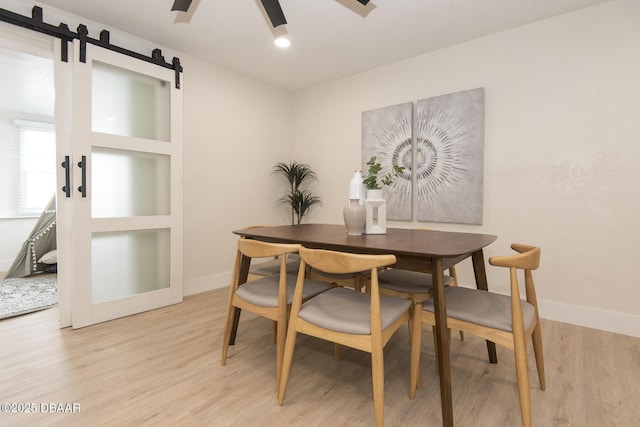 dining space featuring a barn door, ceiling fan, and light hardwood / wood-style flooring