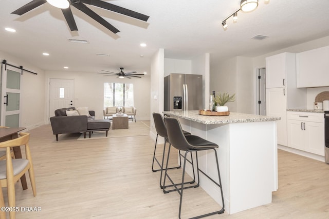 kitchen featuring light hardwood / wood-style flooring, white cabinetry, a kitchen island, stainless steel fridge with ice dispenser, and a barn door