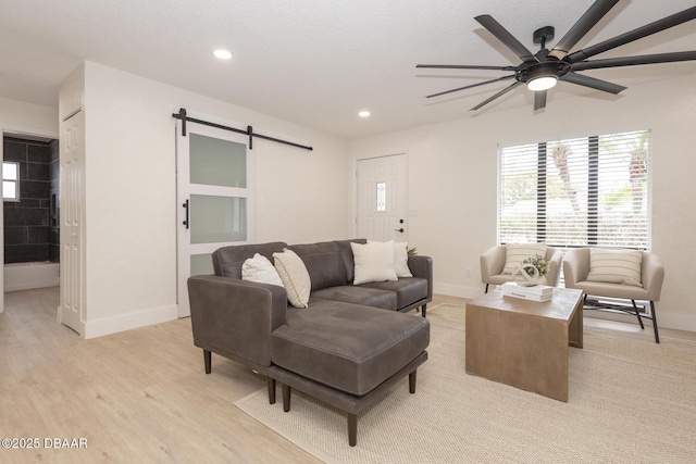 living room featuring a barn door, ceiling fan, and light hardwood / wood-style flooring