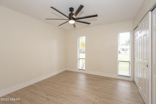 empty room featuring ceiling fan, a wealth of natural light, and light wood-type flooring