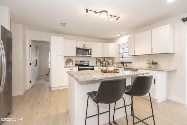 kitchen featuring appliances with stainless steel finishes, light wood-type flooring, a kitchen island, and white cabinets