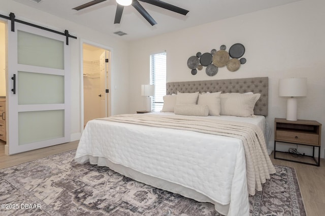 bedroom with ceiling fan, wood-type flooring, a barn door, a spacious closet, and a closet