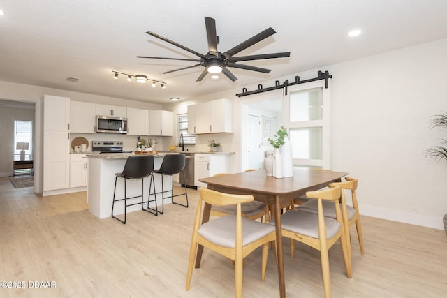 dining area with sink, a barn door, ceiling fan, and light wood-type flooring