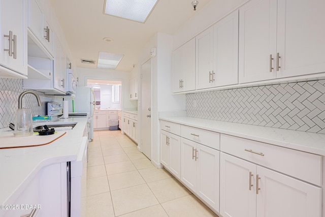 kitchen featuring white appliances, white cabinetry, light tile patterned flooring, and backsplash