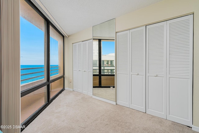 unfurnished bedroom with a textured ceiling, light carpet, and a water view