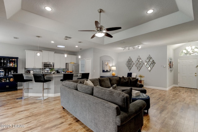 living room with a textured ceiling, a raised ceiling, ceiling fan, and light wood-type flooring