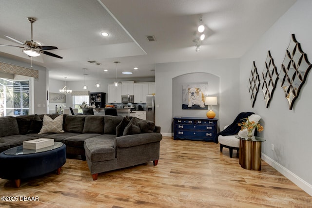 living room featuring ceiling fan with notable chandelier and light hardwood / wood-style flooring