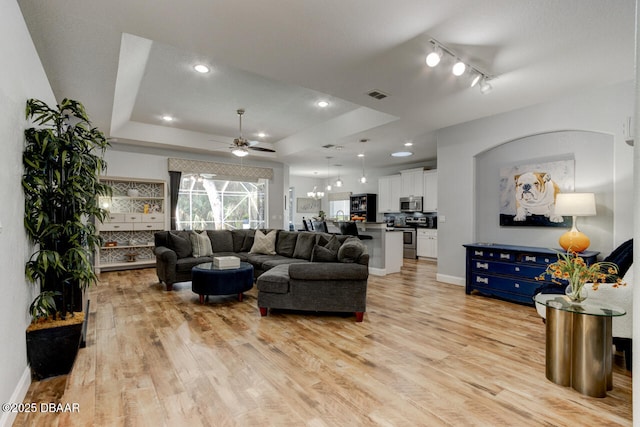 living room with light hardwood / wood-style floors, a raised ceiling, and ceiling fan