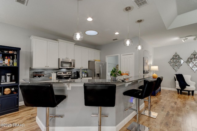 kitchen with stainless steel appliances, white cabinetry, a breakfast bar, and pendant lighting