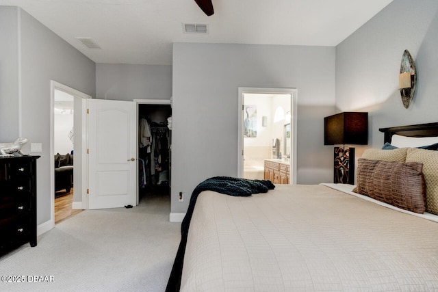 bedroom with ensuite bath, a spacious closet, light colored carpet, a closet, and ceiling fan