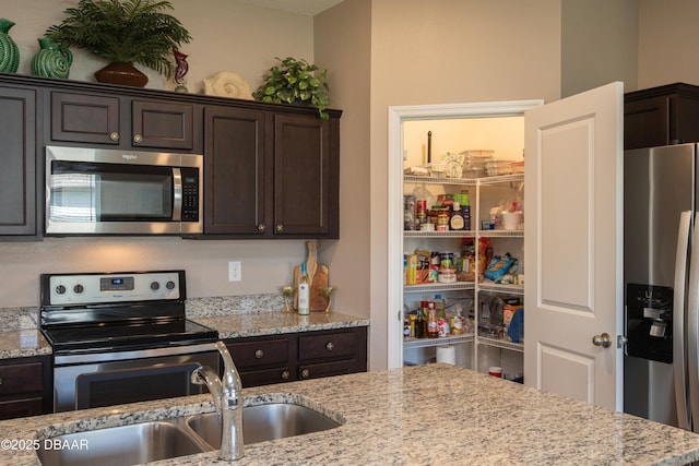 kitchen featuring appliances with stainless steel finishes, a sink, dark brown cabinets, and light stone countertops