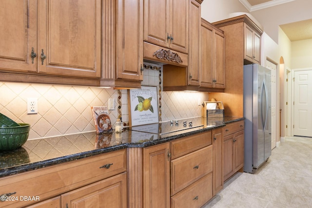 kitchen with dark stone counters, crown molding, stainless steel fridge, tasteful backsplash, and stovetop