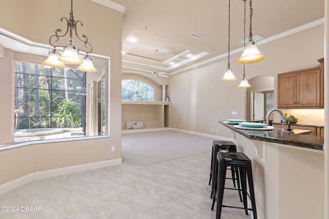 kitchen featuring backsplash, ornamental molding, dark stone counters, a raised ceiling, and hanging light fixtures