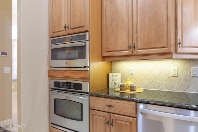 kitchen with stainless steel dishwasher, dark stone countertops, and tasteful backsplash