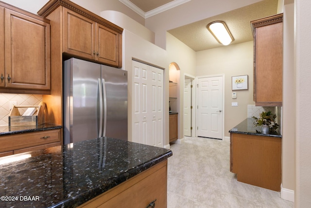 kitchen featuring stainless steel refrigerator, dark stone countertops, a textured ceiling, decorative backsplash, and ornamental molding