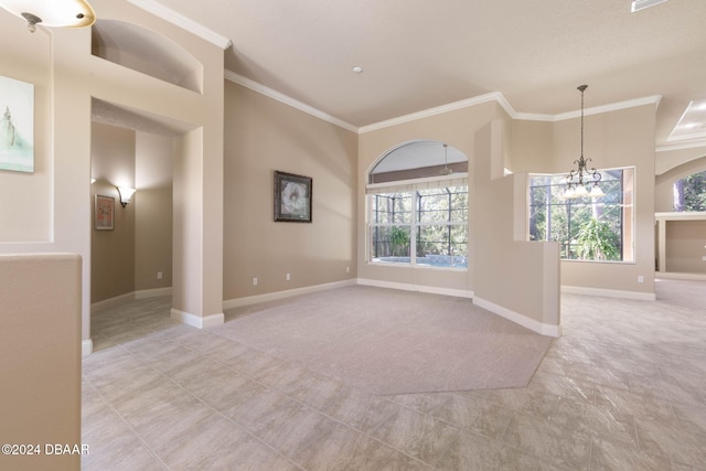 spare room featuring a healthy amount of sunlight, light colored carpet, ornamental molding, and a chandelier