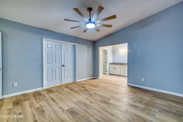 unfurnished bedroom featuring lofted ceiling, baseboards, a sink, and light wood-style floors