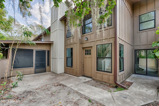 view of exterior entry with board and batten siding and a patio area