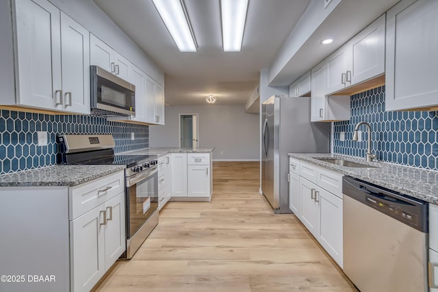 kitchen featuring white cabinets, appliances with stainless steel finishes, a peninsula, light stone countertops, and a sink