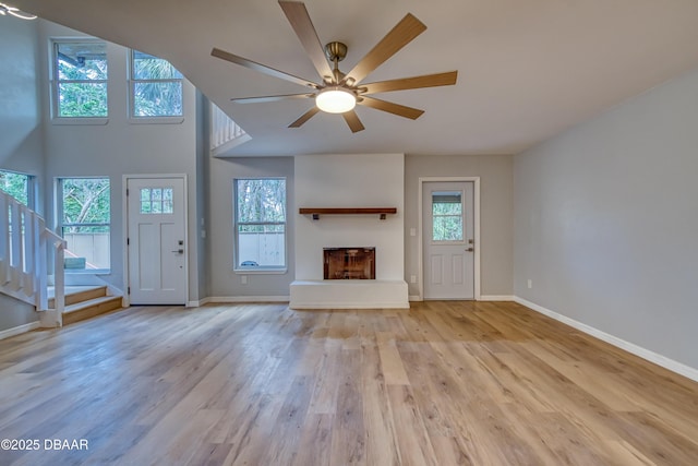 unfurnished living room featuring baseboards, a fireplace with raised hearth, stairway, and light wood finished floors