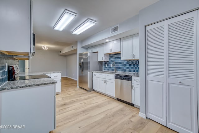 kitchen with stainless steel appliances, light stone counters, tasteful backsplash, light hardwood / wood-style floors, and white cabinets