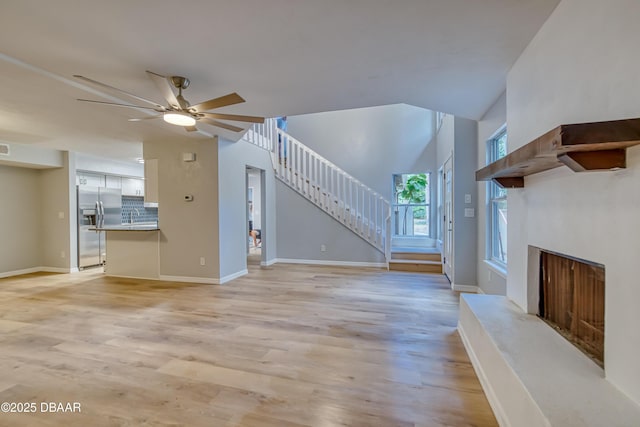 unfurnished living room featuring a premium fireplace, light wood-style floors, ceiling fan, baseboards, and stairs