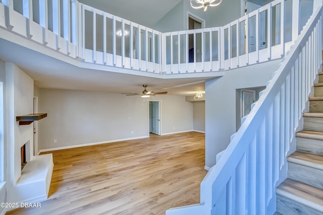 stairs with a high ceiling, baseboards, a fireplace with raised hearth, and wood finished floors