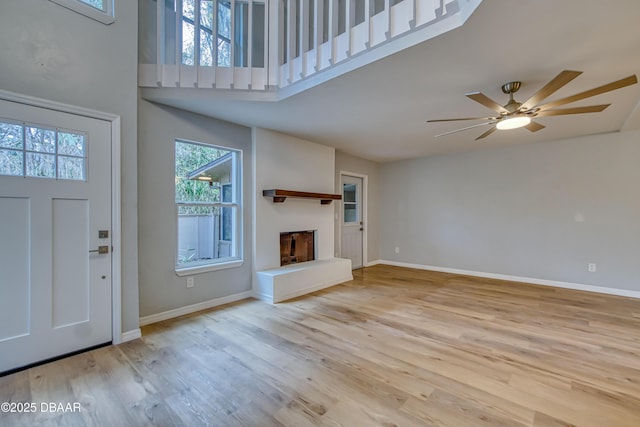 entryway featuring a fireplace with raised hearth, light wood-style flooring, a high ceiling, a ceiling fan, and baseboards