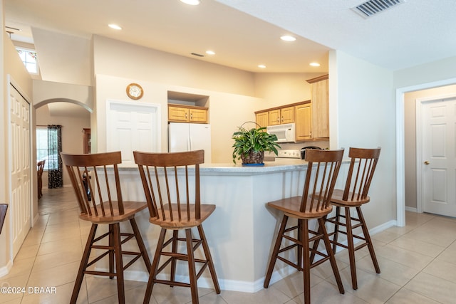 kitchen with kitchen peninsula, white appliances, a breakfast bar area, light brown cabinetry, and light tile patterned floors