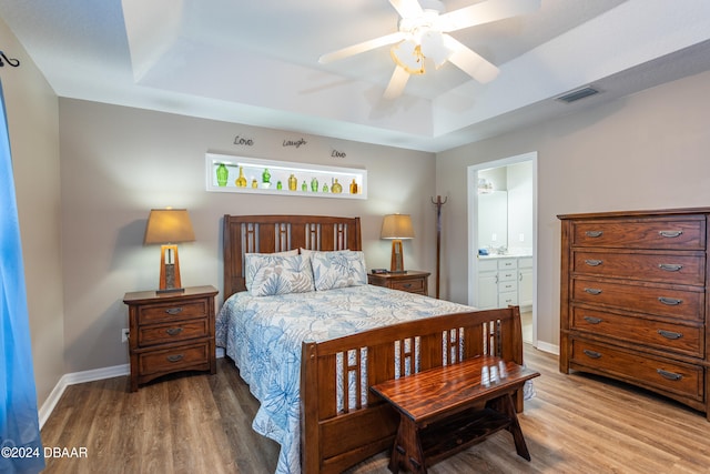 bedroom with a tray ceiling, ensuite bath, ceiling fan, and hardwood / wood-style flooring