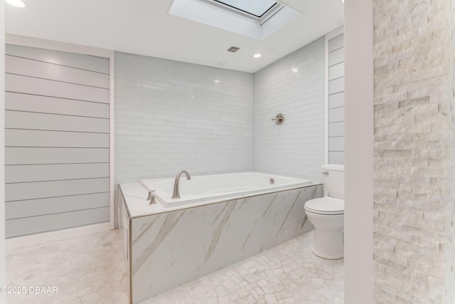 bathroom with a relaxing tiled tub, toilet, and a skylight