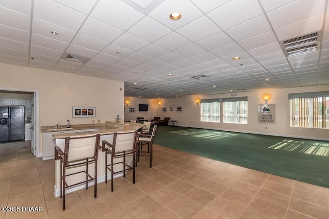 carpeted dining space with golf simulator and a paneled ceiling