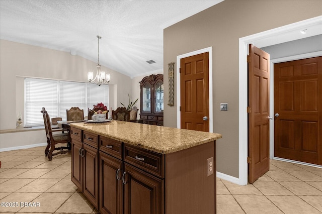 kitchen featuring light tile patterned floors, decorative light fixtures, light stone countertops, vaulted ceiling, and a kitchen island