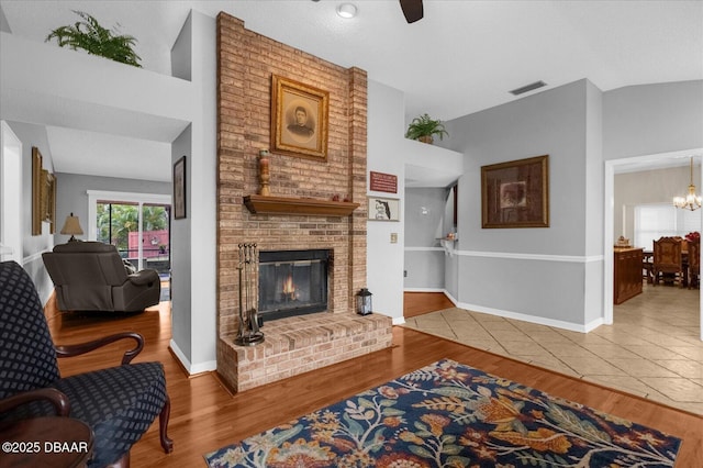 living room featuring lofted ceiling, a fireplace, ceiling fan with notable chandelier, and hardwood / wood-style floors