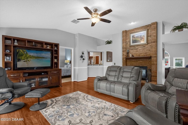 living room with ceiling fan, vaulted ceiling, a fireplace, wood-type flooring, and a textured ceiling