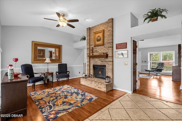 tiled living room featuring ceiling fan, vaulted ceiling, a brick fireplace, and a textured ceiling