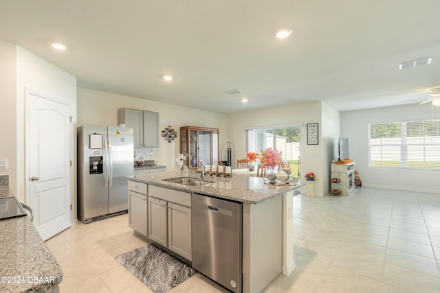 kitchen featuring stainless steel appliances, light stone counters, sink, an island with sink, and gray cabinetry